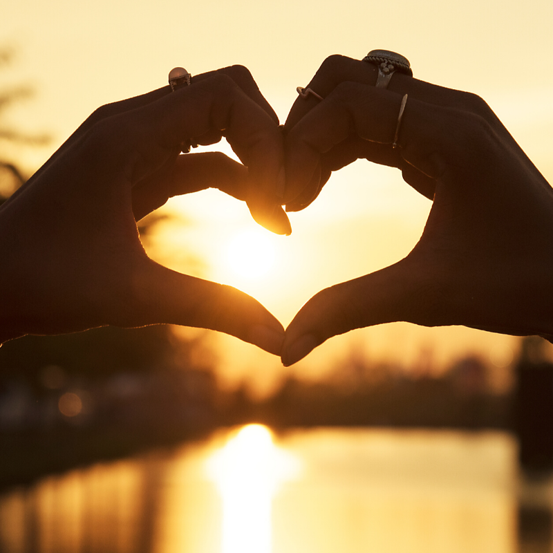 hands in shape of heart at sunset